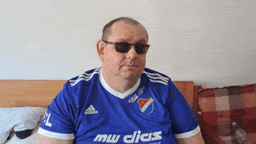 a man wearing a blue adidas shirt sits on a couch