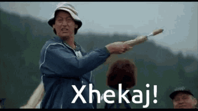 a man is holding a stick with the word xhekaj written on it
