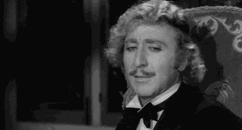 a man in a tuxedo and bow tie is sitting in a chair in a black and white photo .