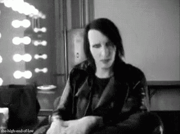 a black and white photo of marilyn manson sitting on a couch in a room .