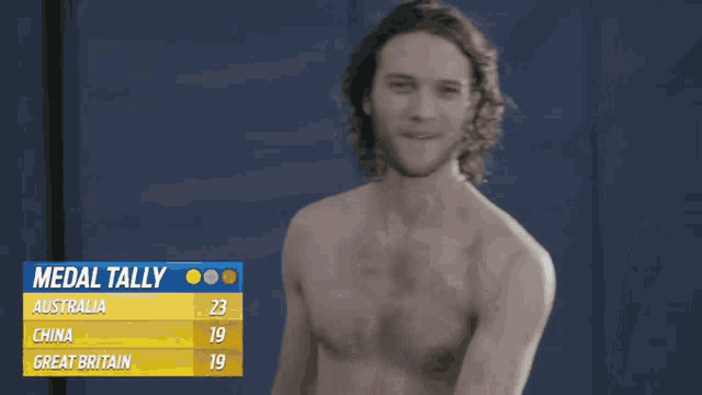 a man without a shirt is standing in front of a medal tally sign