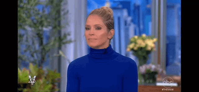 a woman wearing a blue turtleneck sweater is standing in front of a window .
