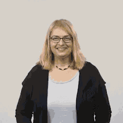 a woman wearing glasses and a black cardigan holds her arms up in the air