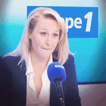 a woman speaking into a microphone in front of a sign that says pe1
