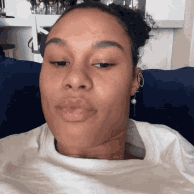 a woman wearing a white shirt and earrings is making a face