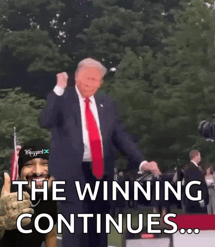 a man in a suit and tie is dancing in front of a sign that says the winning continues ...