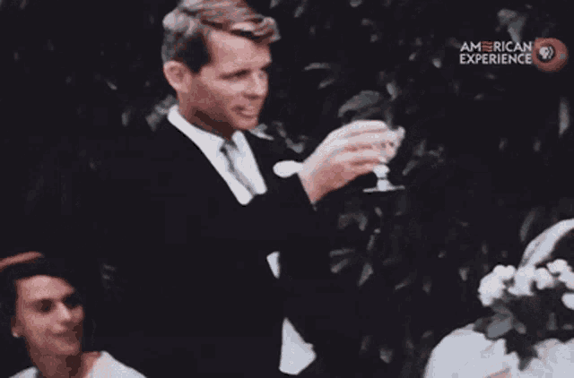 a man in a suit is holding a glass of wine in front of a group of people .