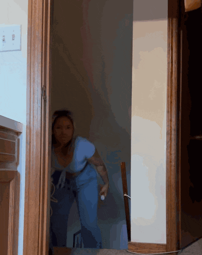 a woman in a blue shirt is standing in a doorway holding a remote control