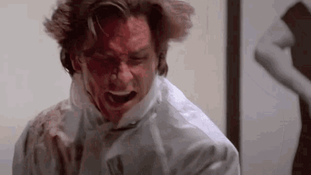 a man with blood on his face is screaming while a woman stands in the background .