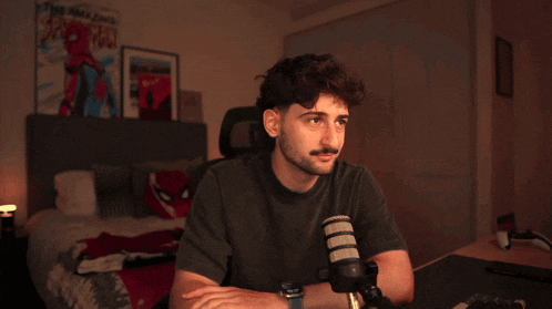 a man with a beard is sitting in a chair in front of a bed