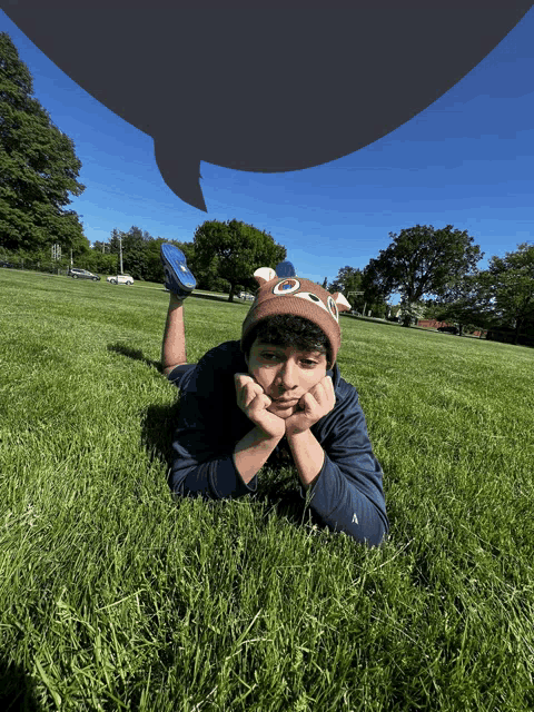 a boy laying on his stomach in the grass with a speech bubble above him