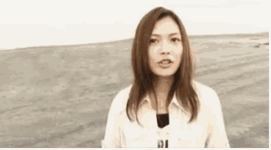 a woman is standing on a beach wearing a white shirt and looking at the camera .