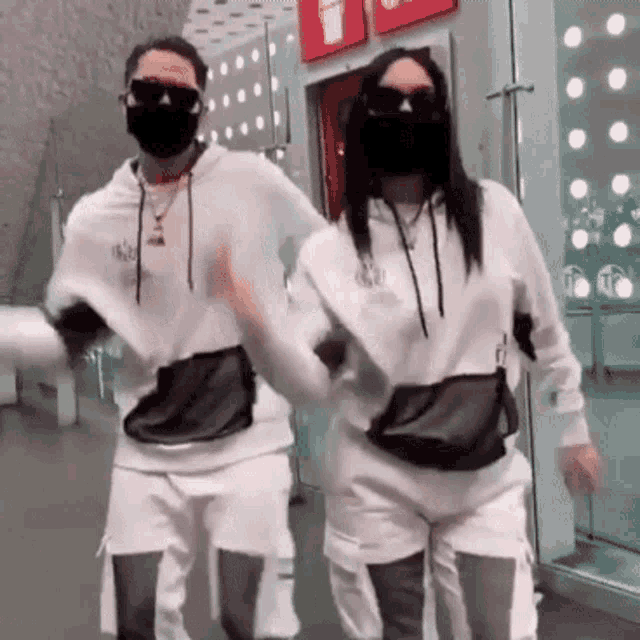 a man and a woman wearing masks and sunglasses are dancing in an airport .