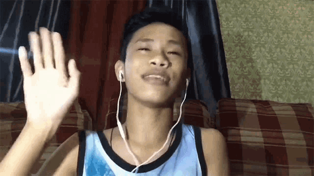 a young man wearing headphones and a blue tank top is waving his hand
