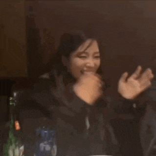 a woman is covering her mouth with her hand while sitting at a table in a dark room .