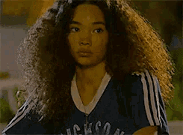 a woman with long curly hair is wearing a blue shirt and a backpack .