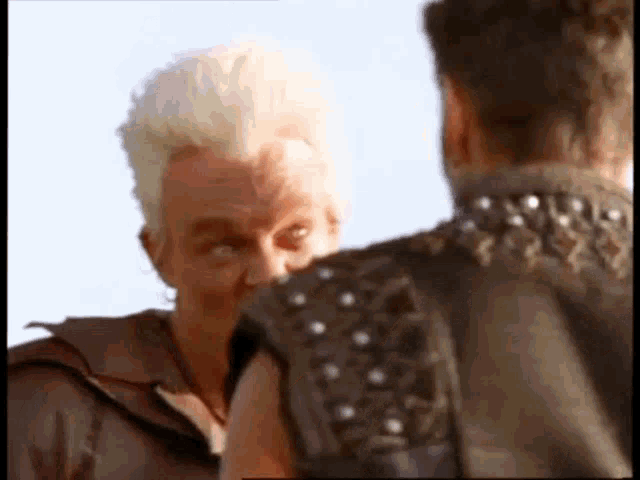 a man with a mohawk is standing next to another man in a leather vest .