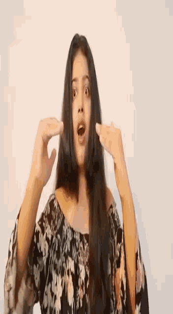 a woman in a floral dress is making a funny face with her hands in front of her face .
