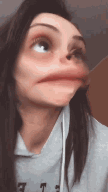 a woman wearing a grey shirt with the letter t on it making a funny face