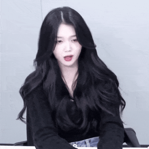 a woman with long black hair is wearing a black shirt and blue jeans
