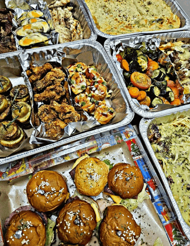 a variety of food in aluminum foil containers including burgers and vegetables