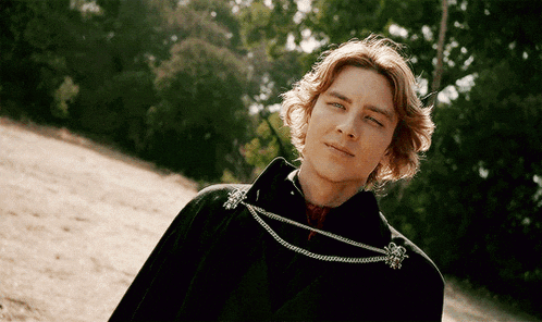 a man wearing a black cape with a silver chain around his neck