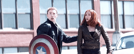 captain america and black widow are standing next to each other on the street .