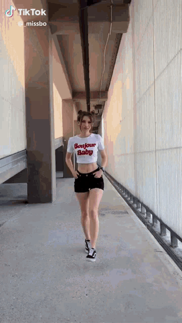 a woman in a bonjour baby crop top and shorts is walking down a hallway .