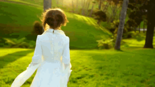 a woman in a white dress is walking through a field