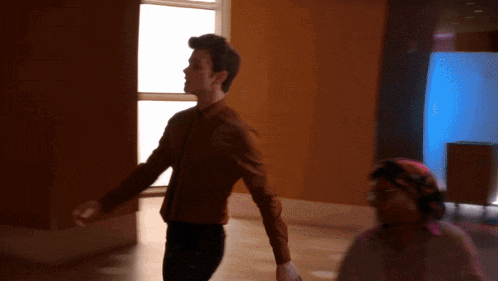 a man in a brown jacket is walking in a room