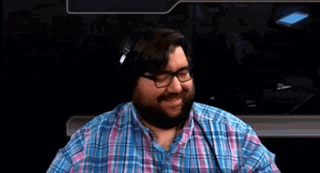 a man with glasses and a beard is waving his hand while wearing headphones .