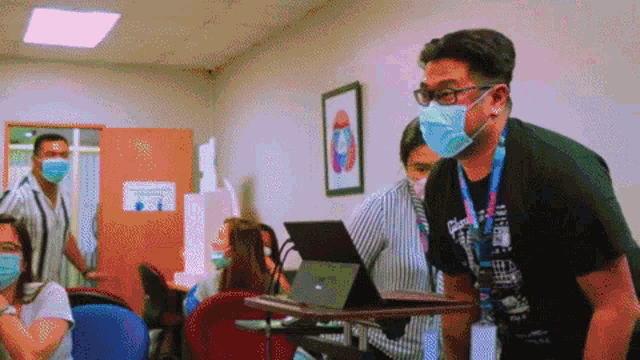 a man wearing glasses and a mask is standing in front of a laptop