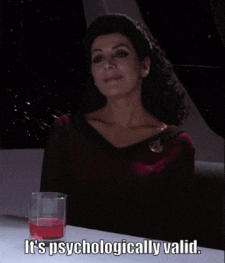 a woman is sitting at a table with a glass of red liquid and the words it 's psychologically valid