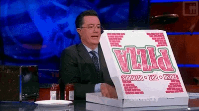 a man in a suit and tie is holding a pizza box that says pizza on it