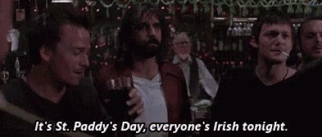 a group of men are standing in a bar drinking beer and smoking cigarettes .