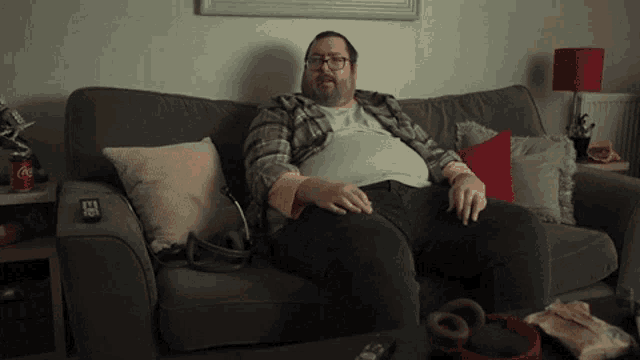 a man sits on a couch with a coca cola can on the arm
