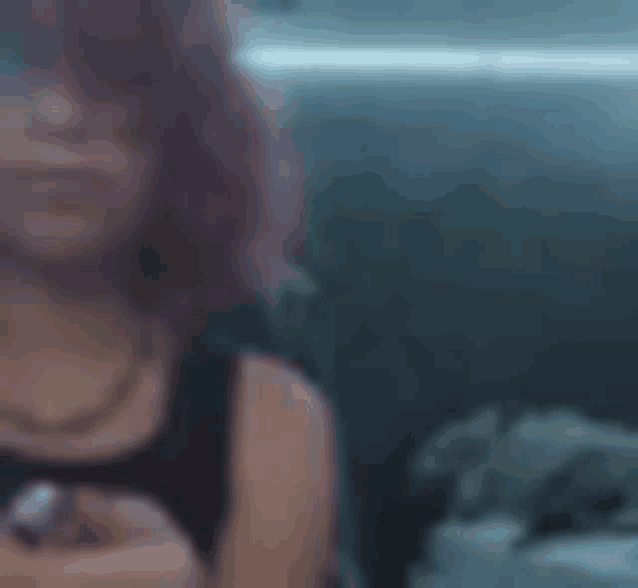 a woman in a black tank top is sitting in a dark room looking at her phone .