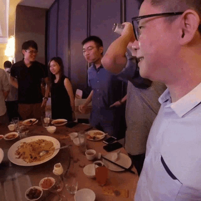 a group of people are gathered around a table with plates of food on it