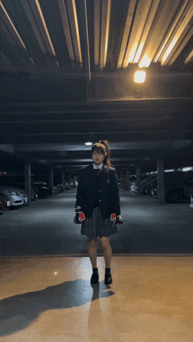 a girl in a school uniform is standing in a parking garage wearing boxing gloves