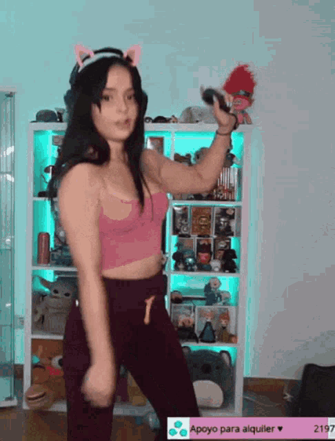 a woman in a pink crop top is dancing in front of a shelf with stuffed animals
