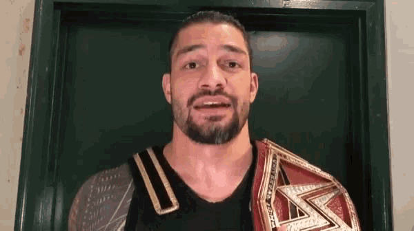 a man with a beard and a wrestling belt is standing in front of a door .