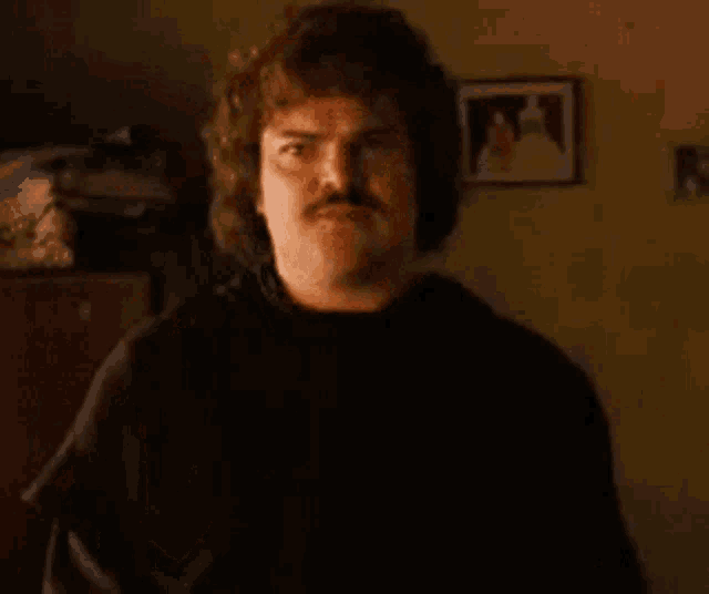 a man with a mustache is standing in a room looking at something .