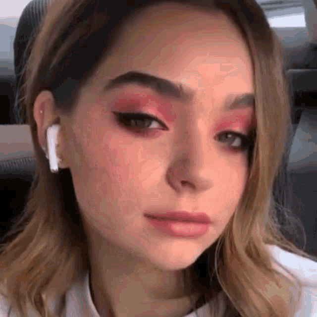 a close up of a woman 's face with red eyeshadow and ear buds .