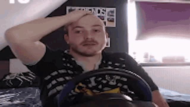 a man is sitting on a bed with a steering wheel on his lap .