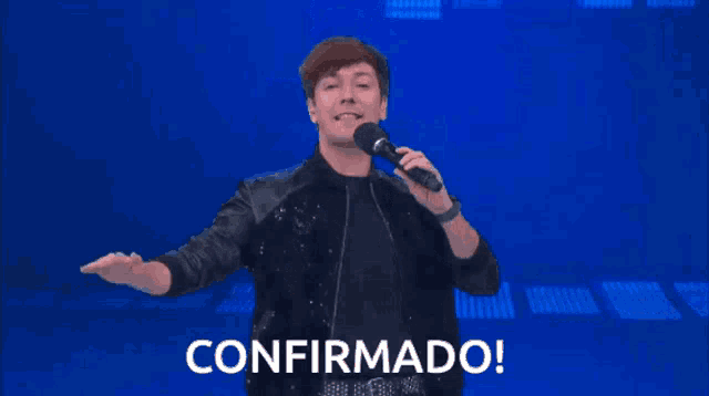 a man singing into a microphone with confirmado written on the screen behind him