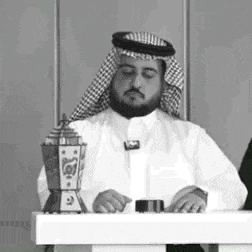 a man with a beard is sitting at a table with a lantern in the background .