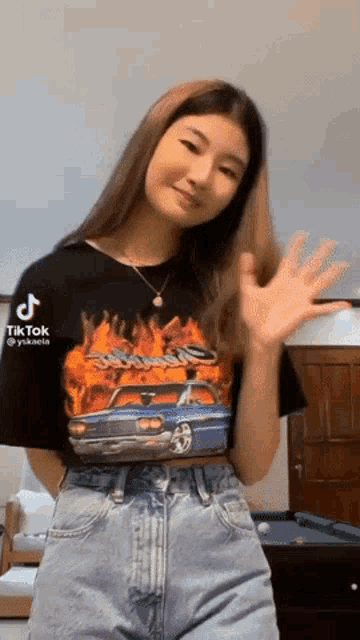 a woman wearing a black t-shirt with a car on it is waving