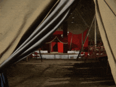 the inside of a circus tent with tables and chairs and a red curtain