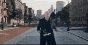 a man in a black coat is walking down a city street .