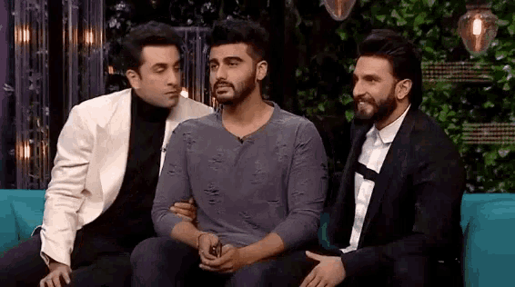 three men are sitting on a blue couch and one of them is hugging another man .